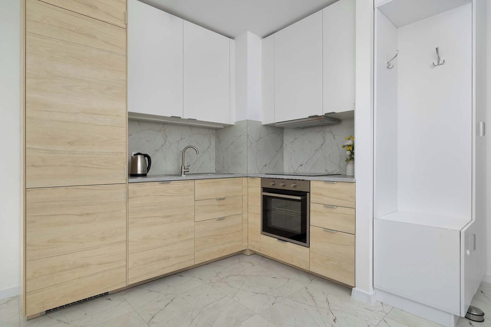 A dedicated entryway nook next to the kitchen features a built-in white wardrobe with a low storage bench. The clean white lines blend seamlessly into the apartment's entry corridor.