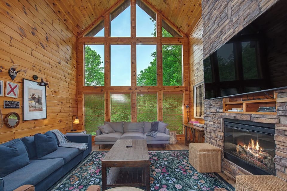 Your living room features soaring windows framing lush forest views, cozy sofas to sink into, and a crackling stone fireplace that sets the perfect mood for mountain evenings.
