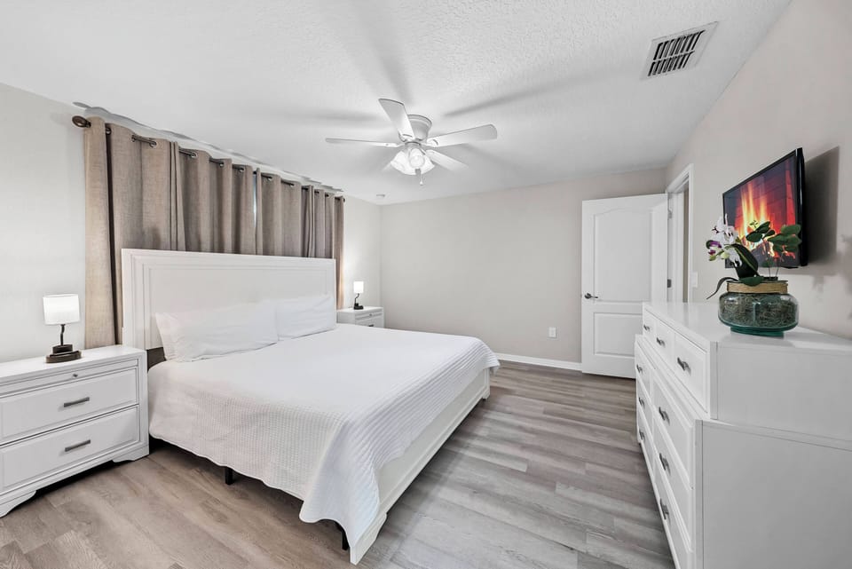 Step into a bright bedroom featuring a spacious white bed framed by soft gray curtains. The sleek dresser and nightstand offer ample storage, while modern decor adds a touch of warmth, creating a restful atmosphere for your stay.