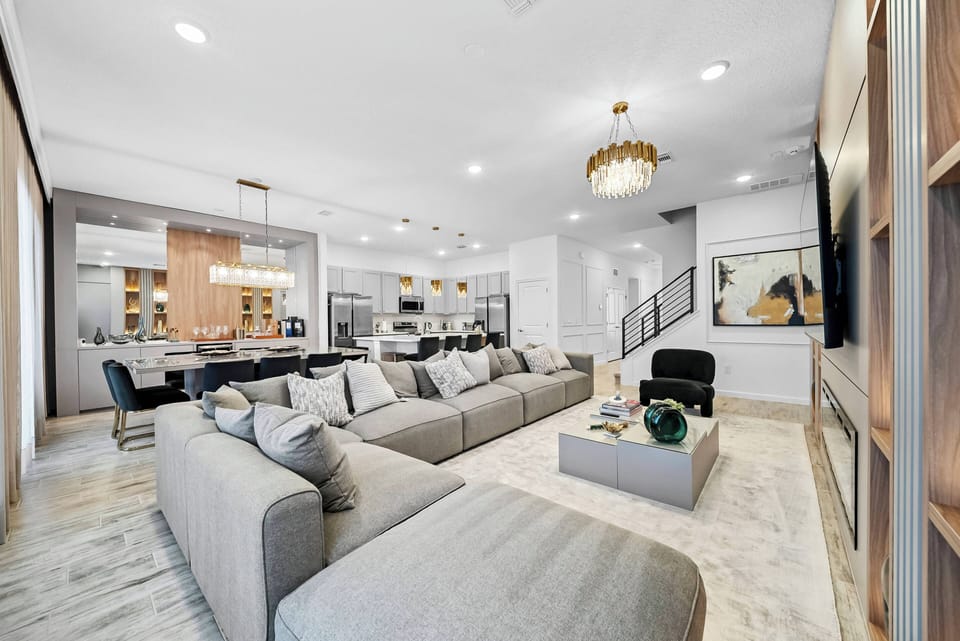 Welcome to a bright living area featuring a cozy gray sectional sofa, ideal for relaxing after your adventures. The elegant chandelier adds warmth to the open layout that flows effortlessly into a chic dining space.