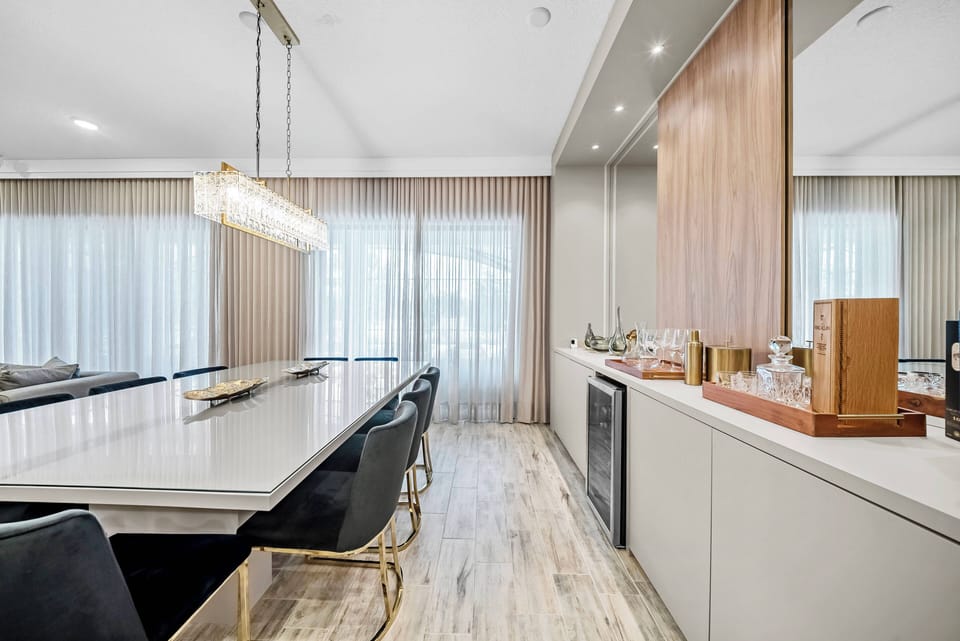 Experience a bright and airy dining area featuring a sleek, white countertop complemented by luxurious black chairs. Floor-to-ceiling curtains allow natural light to flood in, creating a welcoming ambiance perfect for gatherings.