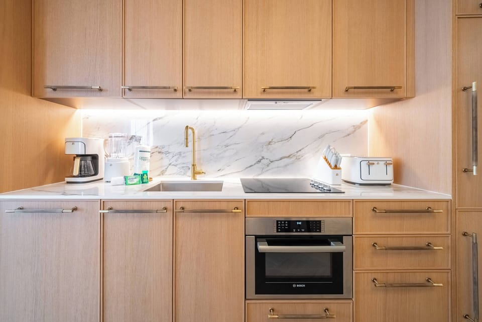This stylish kitchen features warm wood cabinetry and sleek marble accents, creating a sophisticated atmosphere. Modern appliances, including a built-in oven and elegant gold faucet, enhance your culinary experiences in this.