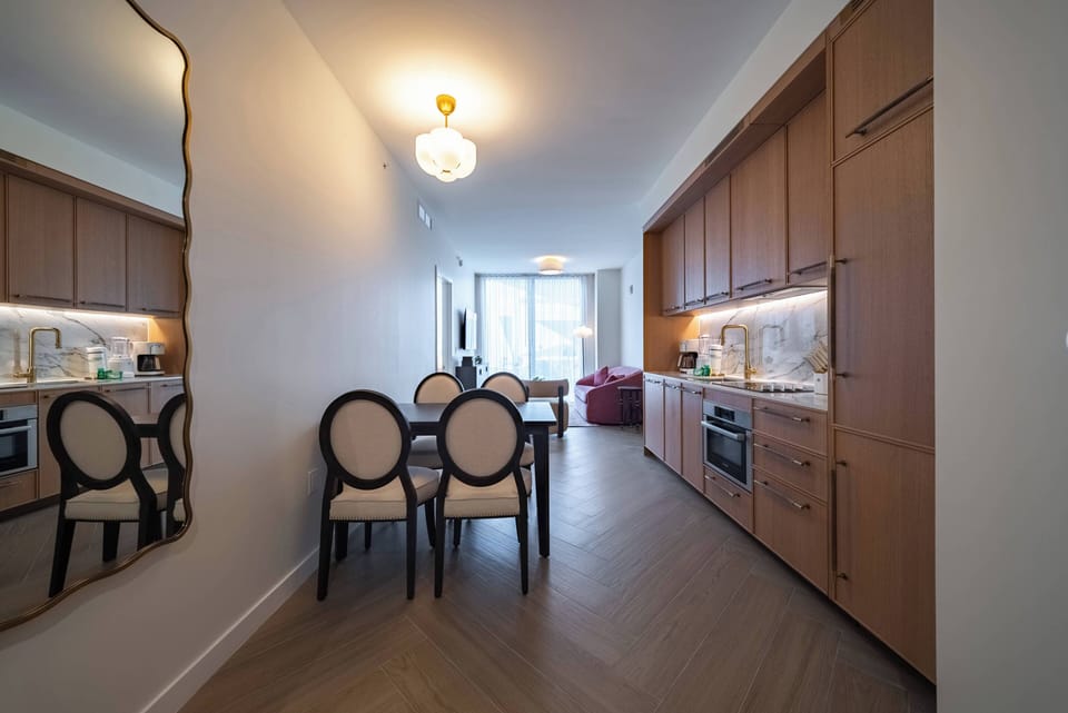 Experience a stylish kitchen with wooden cabinets and a spacious dining area, where warm lighting enhances the elegant mirror and modern appliances, making it perfect for meals, gatherings, and cozy relaxation.