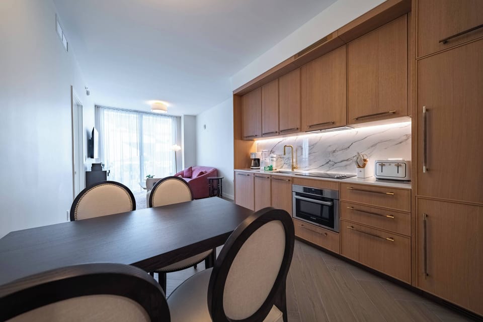 Step into a cozy kitchen featuring warm wooden cabinetry and sleek marble countertops, perfect for preparing meals or enjoying coffee. The soft natural light pours in, inviting relaxation at the stylish dining table set for four.