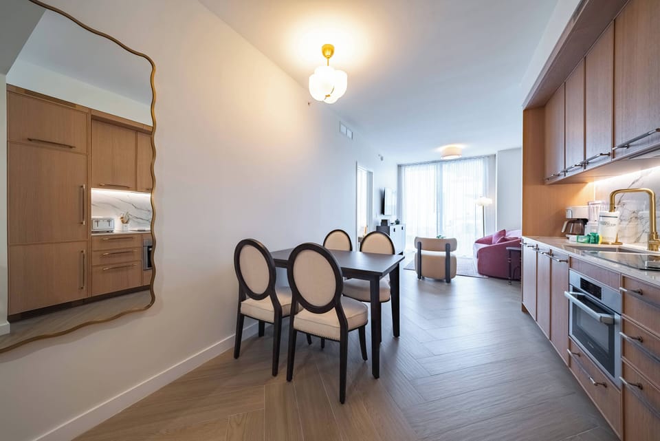 This bright and airy dining area features a sleek wooden table with elegant upholstered chairs, ideal for gatherings. The warm cabinetry and stylish mirror create a welcoming atmosphere to enhance your stay.