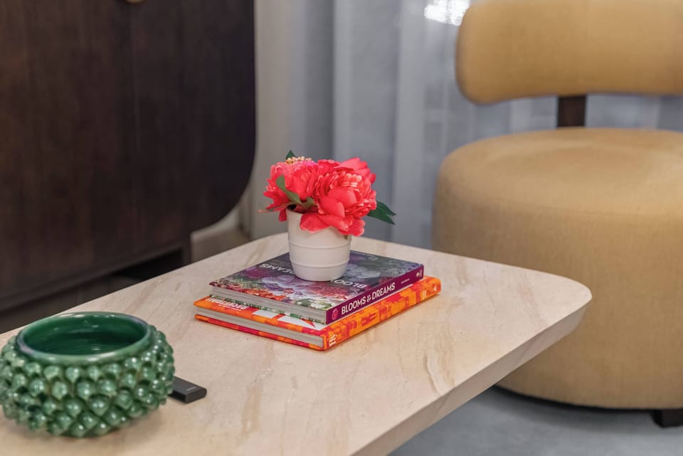This cozy living area boasts a beautiful marble coffee table adorned with colorful books and a lovely floral arrangement, perfectly paired with a stylish beige chair and a unique green bowl that adds warmth and charm.