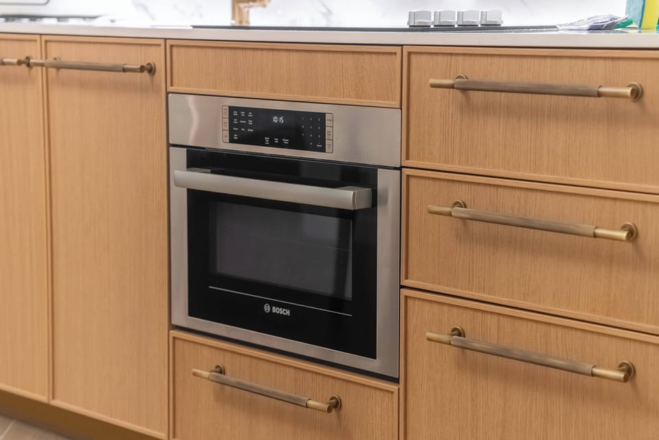Experience a chic kitchen with elegant wood cabinetry and modern metallic accents. The built-in oven adds convenience, and the minimalist design creates a warm, contemporary space perfect for your culinary adventures.