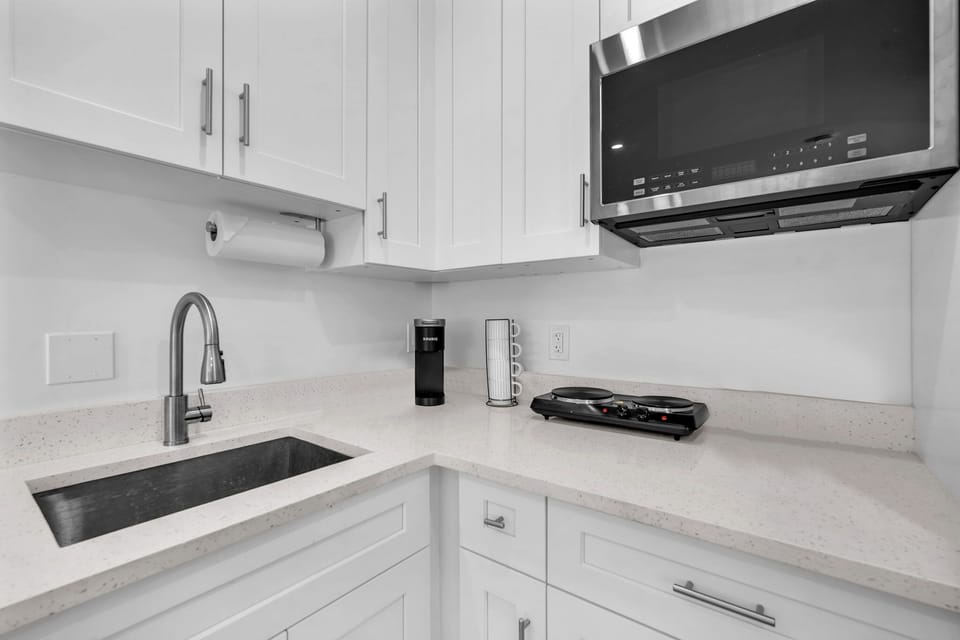 Compact kitchenette with a refrigerator, two-burner electric stove, microwave, Keurig, and ample cabinet storage for short or long stays.