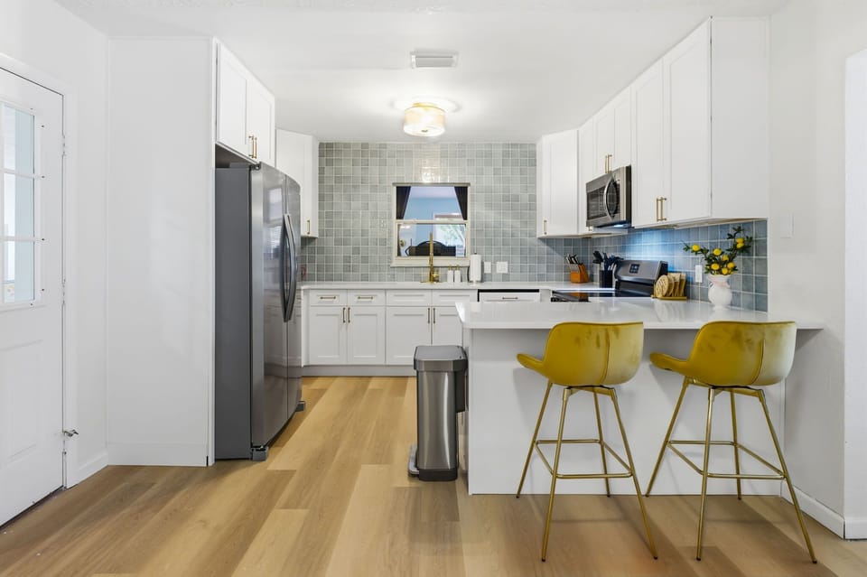 A chef's dream kitchen! 🍳✨ Fully equipped with modern stainless steel appliances, crisp white cabinetry, and an elegant tiled accent wall. The open layout and breakfast bar seating make cooking together a breeze.