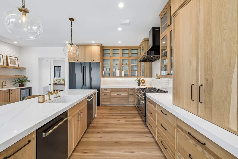 You'll love preparing meals in this spacious, beautifully designed kitchen featuring warm wood cabinetry, sleek white countertops, modern appliances, and elegant pendant lighting that creates the perfect cooking atmosphere.