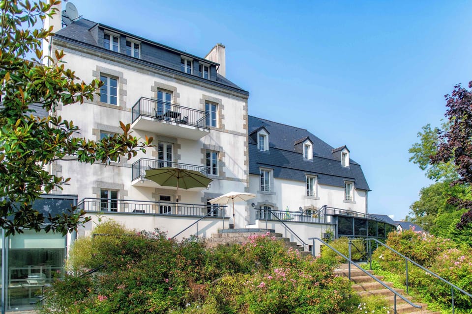 The stone-and-render façade of Le Manoir rises above a manicured garden — your home base a short walk from Pont-Aven's galleries.