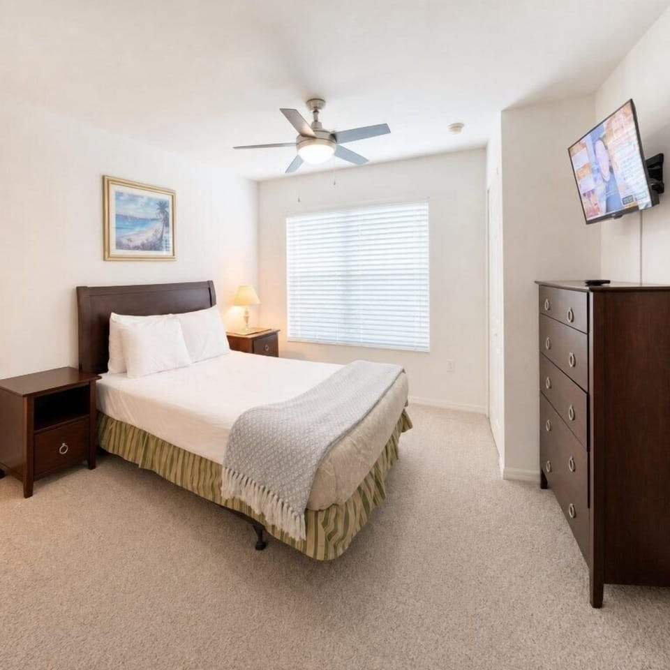 Cozy bedroom with plush bedding, ceiling fan, and flat-screen TV for relaxing evenings.