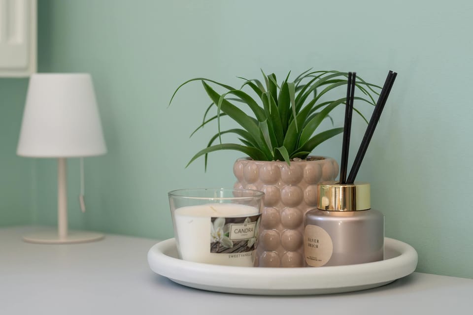 A decorative arrangement featuring a potted plant, candles, and a lamp. Soft colors add a stylish touch to the room.