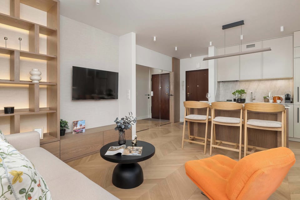A modern open-plan living area combines a lounge, dining space, and kitchen. Warm wooden accents, comfortable seating, and large windows create a bright and welcoming atmosphere.