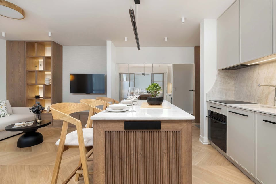 An open-plan living area combines a compact kitchen, dining space, and lounge zone. Wooden finishes and modern furnishings create a functional and elegant environment for everyday living.
