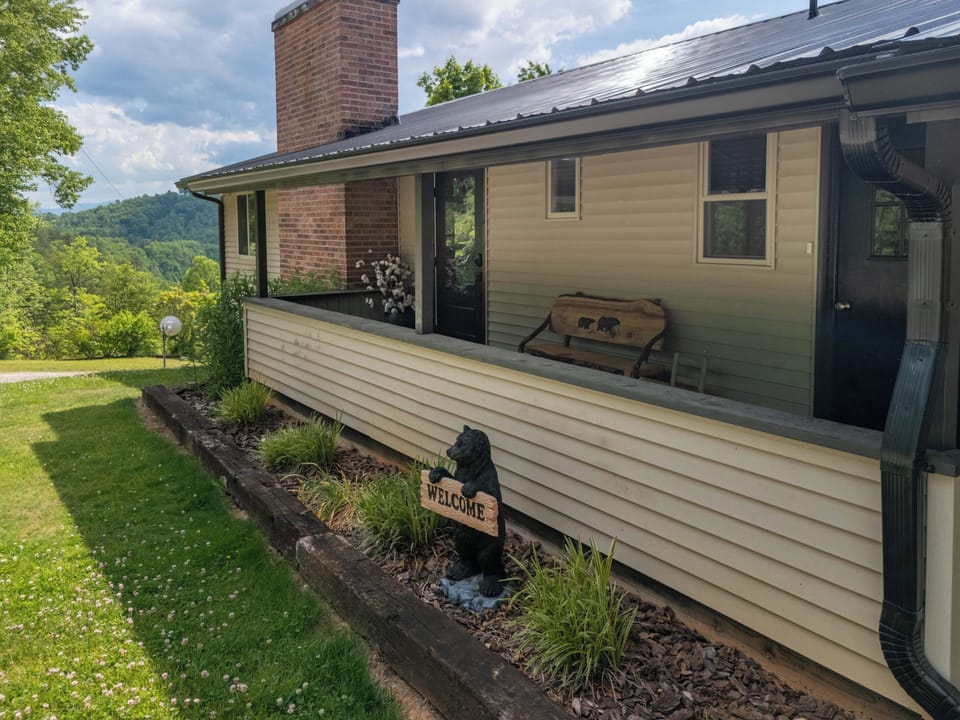 Front Porch – Bear Welcome Sign and Bench - Charming front porch entrance with a carved black bear welcome statue, a bear bench, and mountain views from the railing.