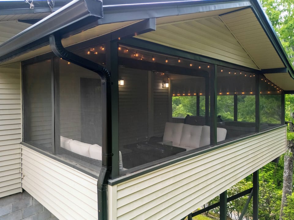 Screened Porch – Exterior Close-Up with String Lights - Close exterior view of the screened porch with string lights, white cushioned sectional sofa, and fire table visible inside.