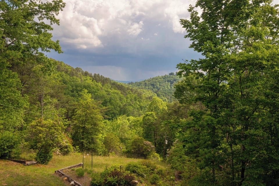 Deck View – Forested Mountain Valley with Storm Clouds - Scenic view from the deck showing a deep forested valley between two mountain ridges under dramatic storm clouds.