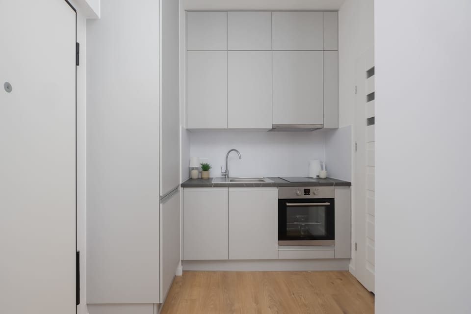 A small contemporary kitchenette with white cabinets, integrated appliances, and clean minimalist lines. Bright lighting enhances the simple functional layout.