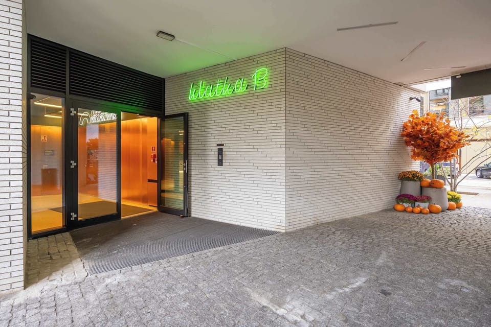 A covered entrance area to a modern residential building featuring illuminated signage and decorative landscaping. Contemporary architecture frames the spacious entryway.