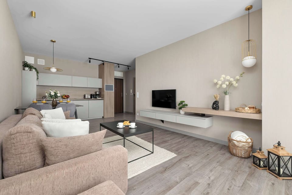 A wide perspective from the living area highlights a low-profile white floating media console adorned with decorative vases. In the background, the apartment opens up seamlessly into the kitchen area.