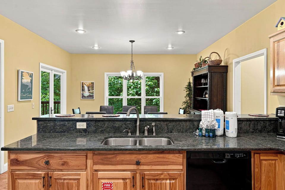 Your fully equipped kitchen features granite countertops, stainless steel sink, and warm wood cabinetry—perfect for preparing home-cooked meals with natural light streaming through windows overlooking lush greenery.
