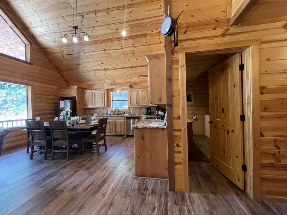 Gather around your dining table in this warm, open-concept space where natural wood surrounds you. The full kitchen invites your culinary adventures, while sunlight streams through large windows.