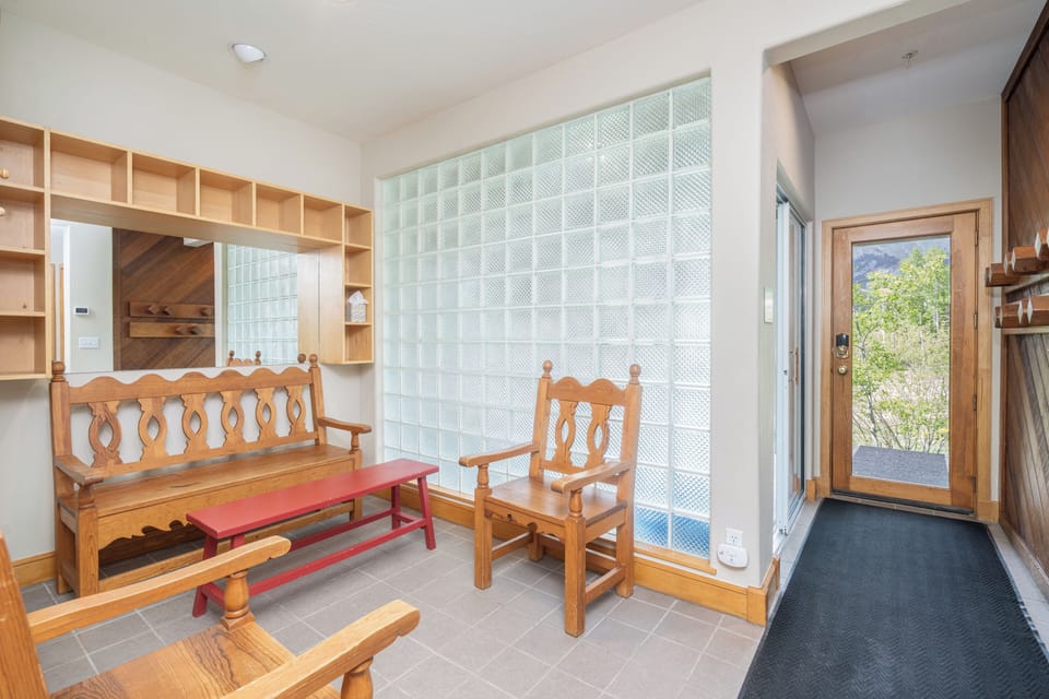 Step into your welcoming entryway with charming wooden bench seating, custom shelving for your belongings, and plenty of natural light from the glass block wall creating a bright, inviting arrival.
