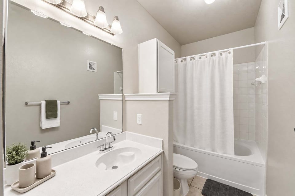 Clean bathroom with a spacious vanity, large mirror, sink, tub and shower combination, toilet, and neatly arranged countertop essentials.