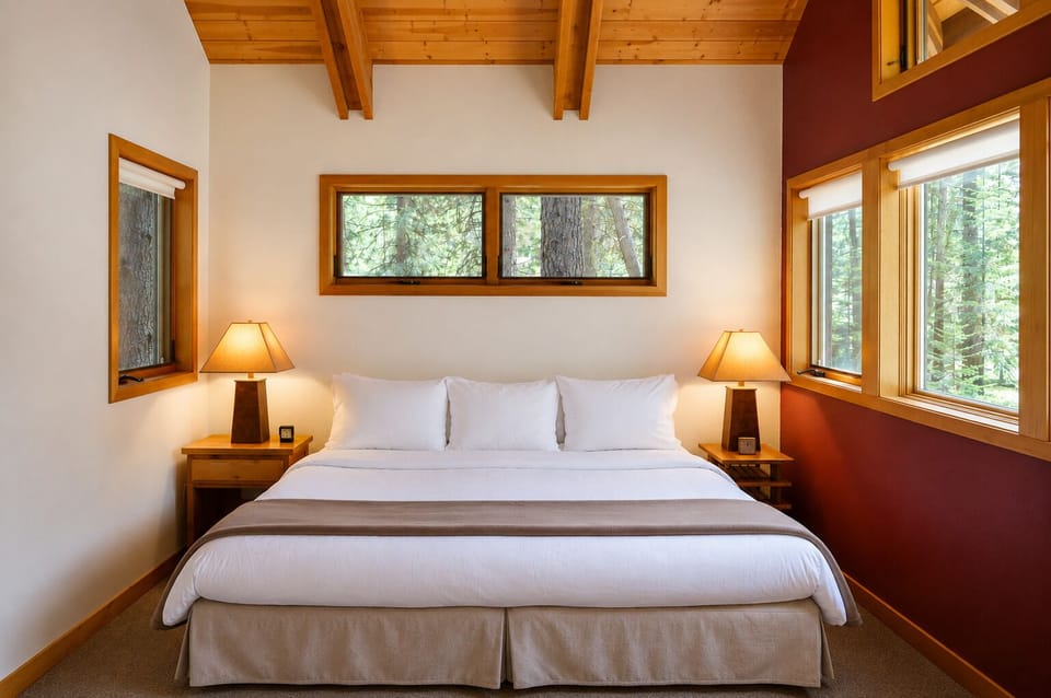 Unwind in your serene retreat with vaulted wood beam ceilings, plush bedding, and towering windows framing tranquil forest views—your peaceful mountain escape awaits.