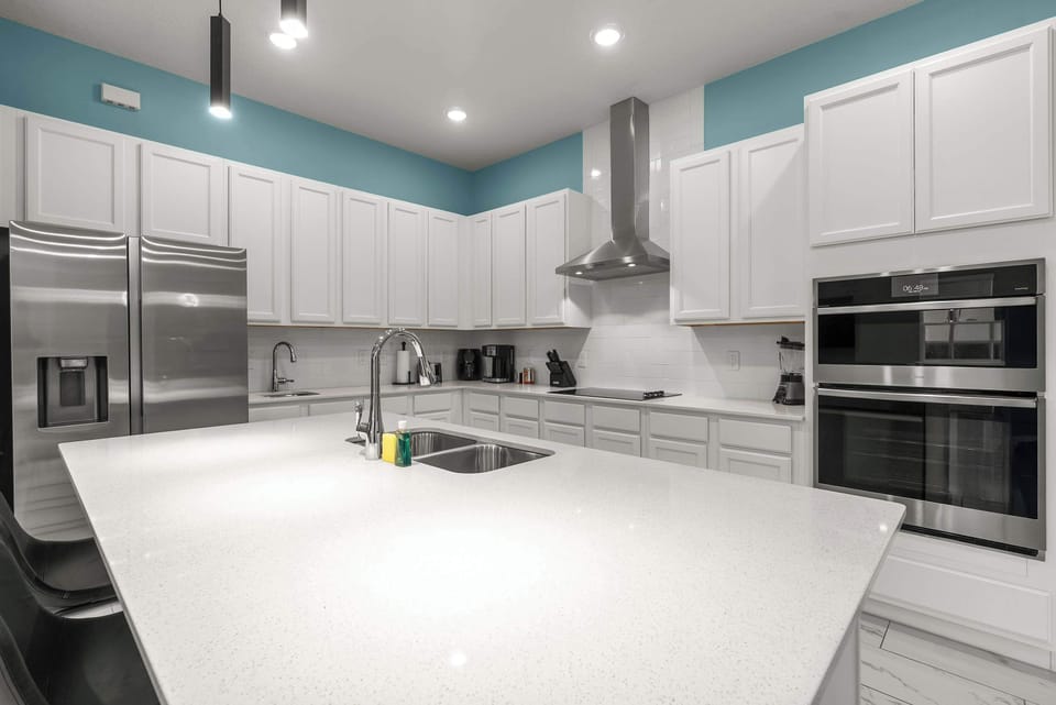 Modern kitchen with a large island, stainless steel appliances, and white cabinetry.