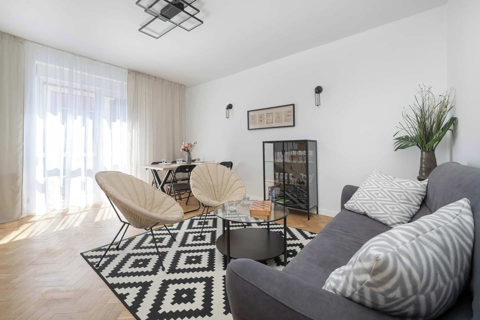 Bright and cozy living room with a gray sofa bed, modern armchairs, and a stylish black-and-white rug.
