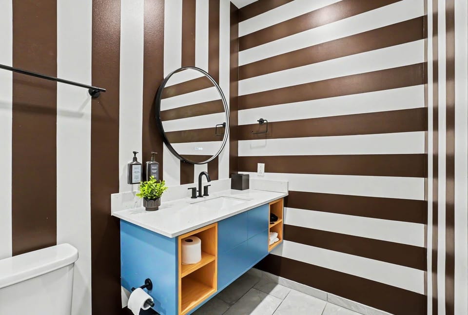 Unit 2: Primary en-suite bathroom with bold striped walls, a spacious single vanity, sleek glass walk-in shower, and stylish finishes that make getting ready feel a little more fun.