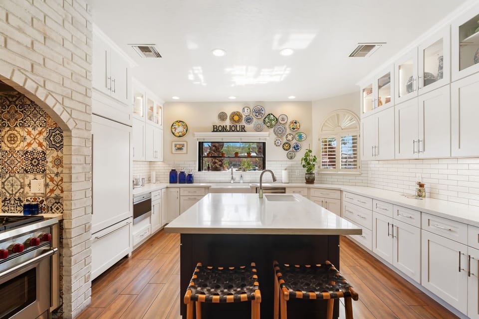 Bright chef’s kitchen with a Wolf range, bold tile backsplash, spacious island with seating, and generous counter space for effortless meals.