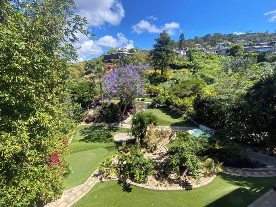 Overlook the beautifully landscaped backyard featuring lush tropical gardens, winding pathways, and multiple private putting greens in a peaceful hillside setting.