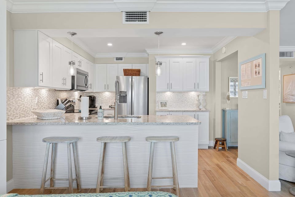 Prepare meals with ease in this modern beach stay kitchen featuring stainless steel appliances, granite countertops, bar seating, and bright coastal finishes perfect for relaxing seaside getaways.