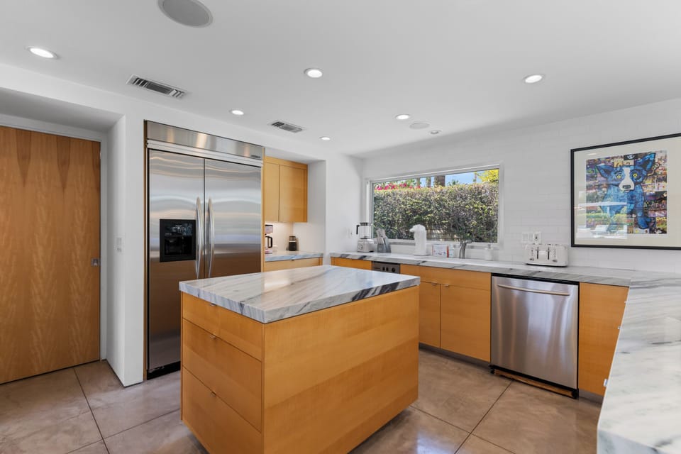 Modern chef's kitchen with a waterfall marble counter, kitchen island, stainless-steel appliances, wine fridge, wet bar, and kitchen essentials.