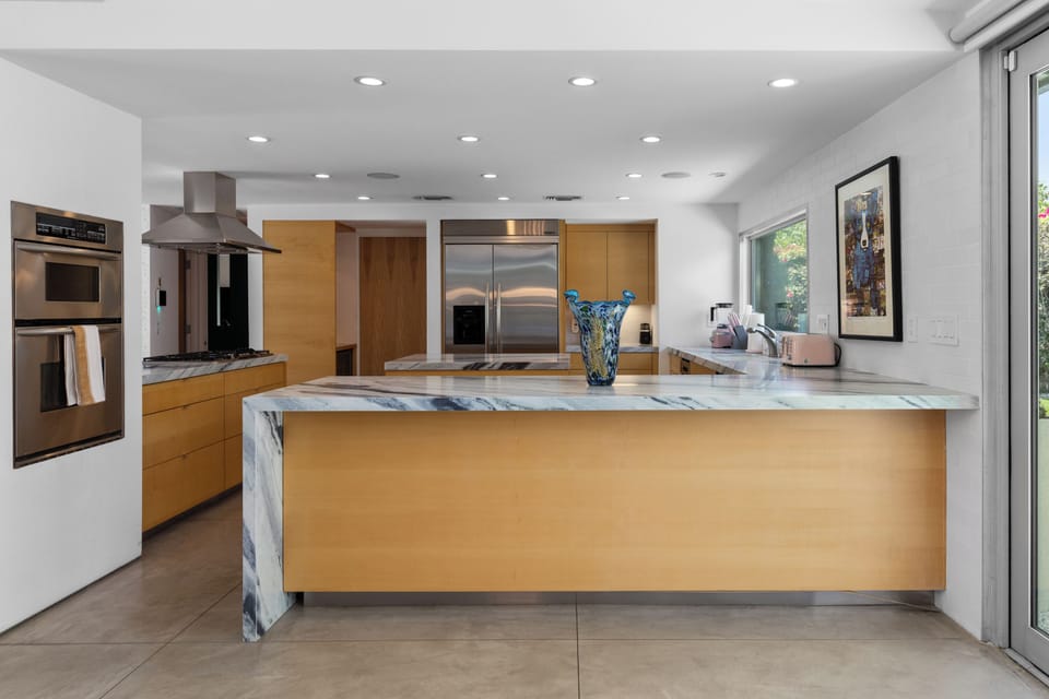 Modern chef's kitchen with a waterfall marble counter, kitchen island, stainless-steel appliances, wine fridge, wet bar, and kitchen essentials.