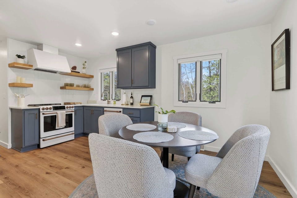 Picture yourself here: a bright kitchen and dining space where you can prepare meals together on modern appliances, gather around the cozy table, and enjoy woodland views from every window.