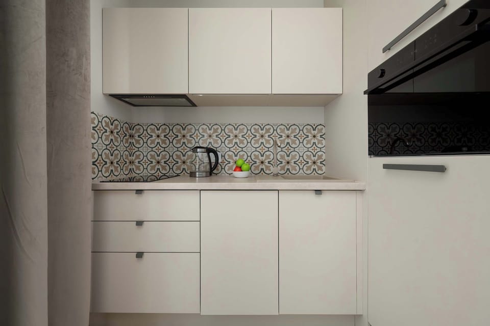 A minimalist kitchen with white cabinetry, patterned backsplash tiles, and integrated appliances. Neutral colors and streamlined finishes give the space a polished appearance.