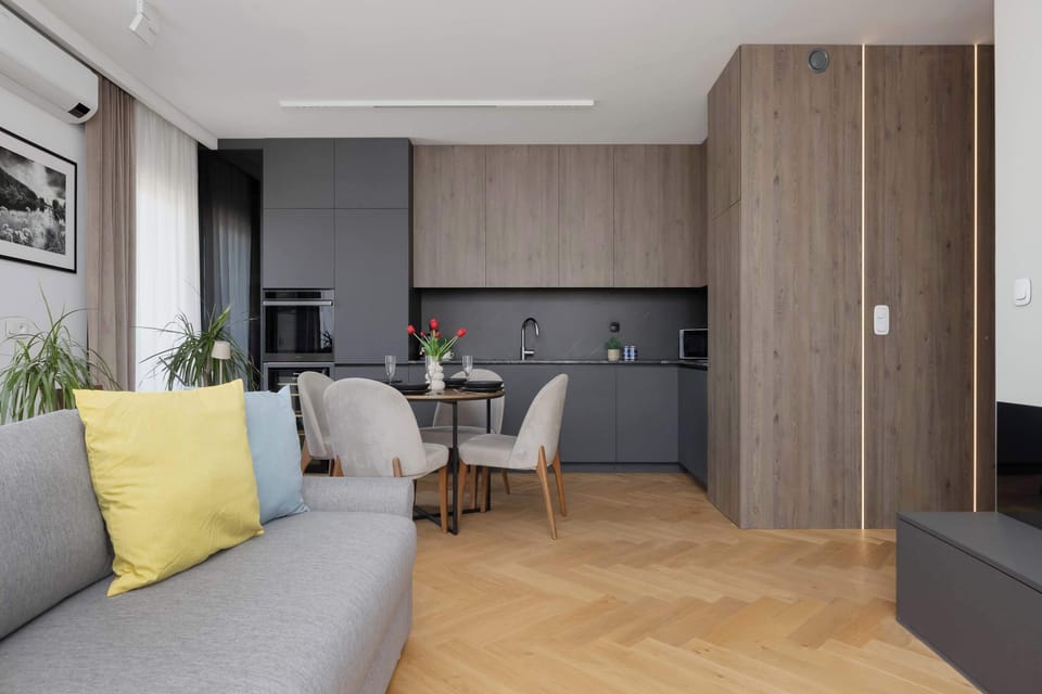 An open-plan living space with a sofa, dining table, and kitchenette. Light wood finishes create a warm atmosphere.