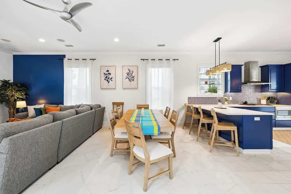 An alternative look at the spacious open-concept layout. This view focuses on the integration of the plush family room, the classic wooden dining table, and the vibrant blue kitchen area.