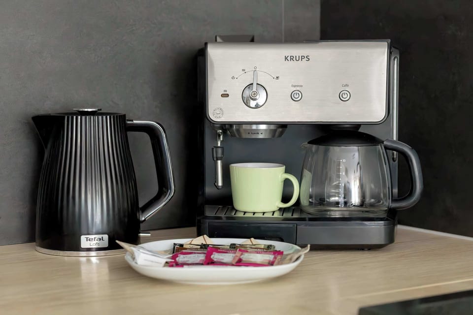 A coffee machine and electric kettle placed on the kitchen countertop. Cups and coffee accessories are ready for use.