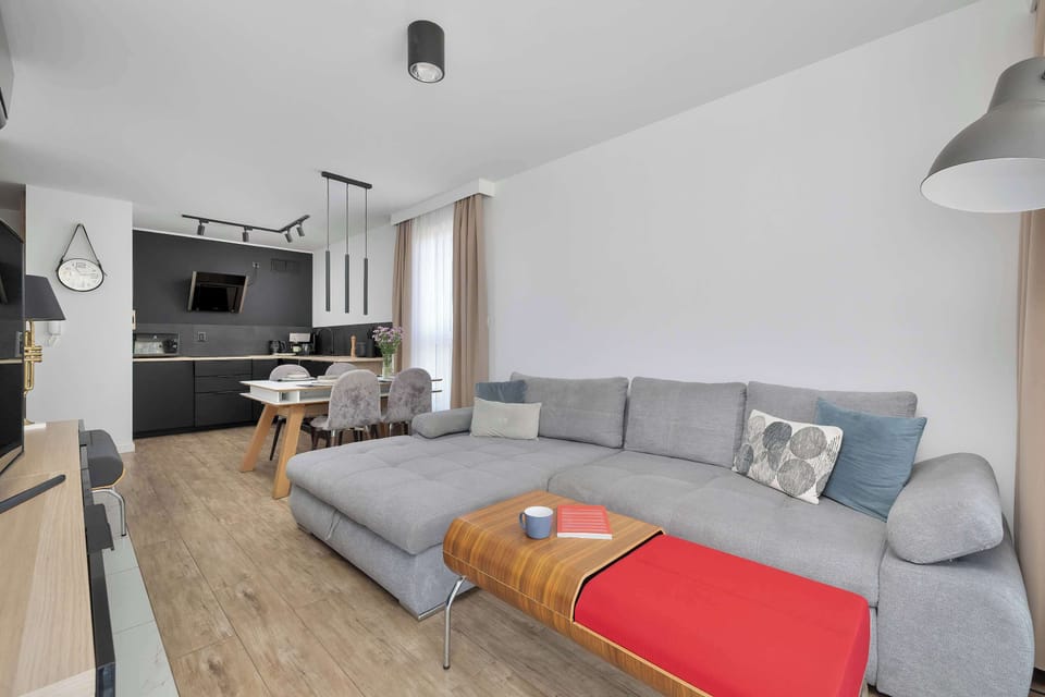 An open-plan living room connected to a modern kitchen. The gray sofa and colorful throw add a welcoming touch.