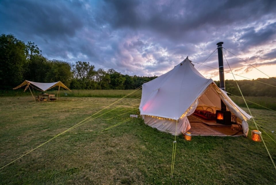Bell tent with woodburner and fairy lights against a fiery sunset sky