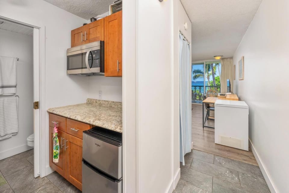 Your private kitchenette features granite counters, warm wood cabinetry, and modern appliances—perfect for preparing light meals while enjoying ocean breezes through the open doorway.