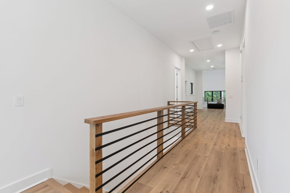 A sunlit hallway with sleek railings and warm wood floors invites you to explore your home's open, modern design.