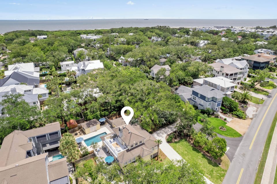 Aerial view captures a coastal neighborhood with lush greenery and ocean views, where this vacation rental is nestled among mature trees near the water.