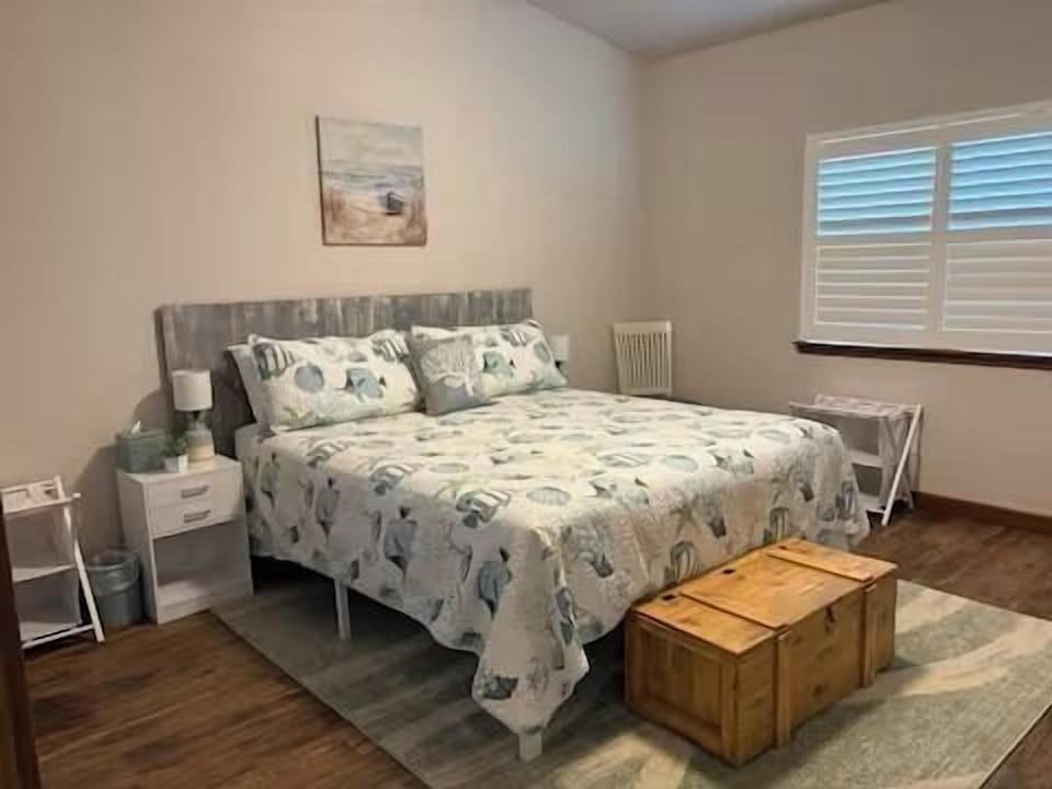 Bright coastal-style bedroom master bedroom with comfy king bed and natural light. Bed side tables have USB ports for device charging.
