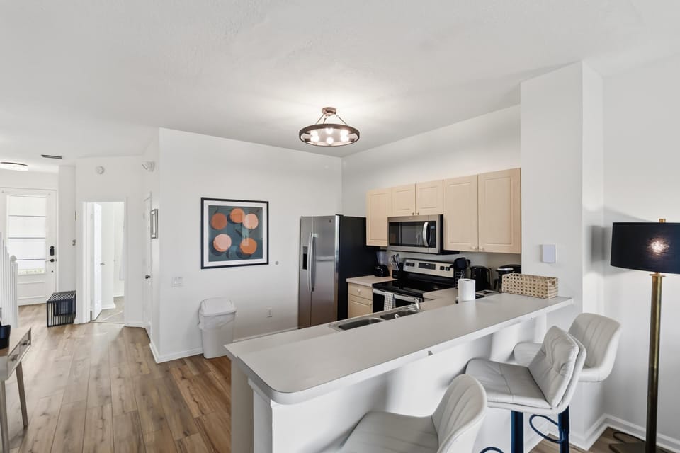 Light wood cabinets and stainless steel appliances frame the kitchen with a white breakfast bar and cushioned swivel stools.
